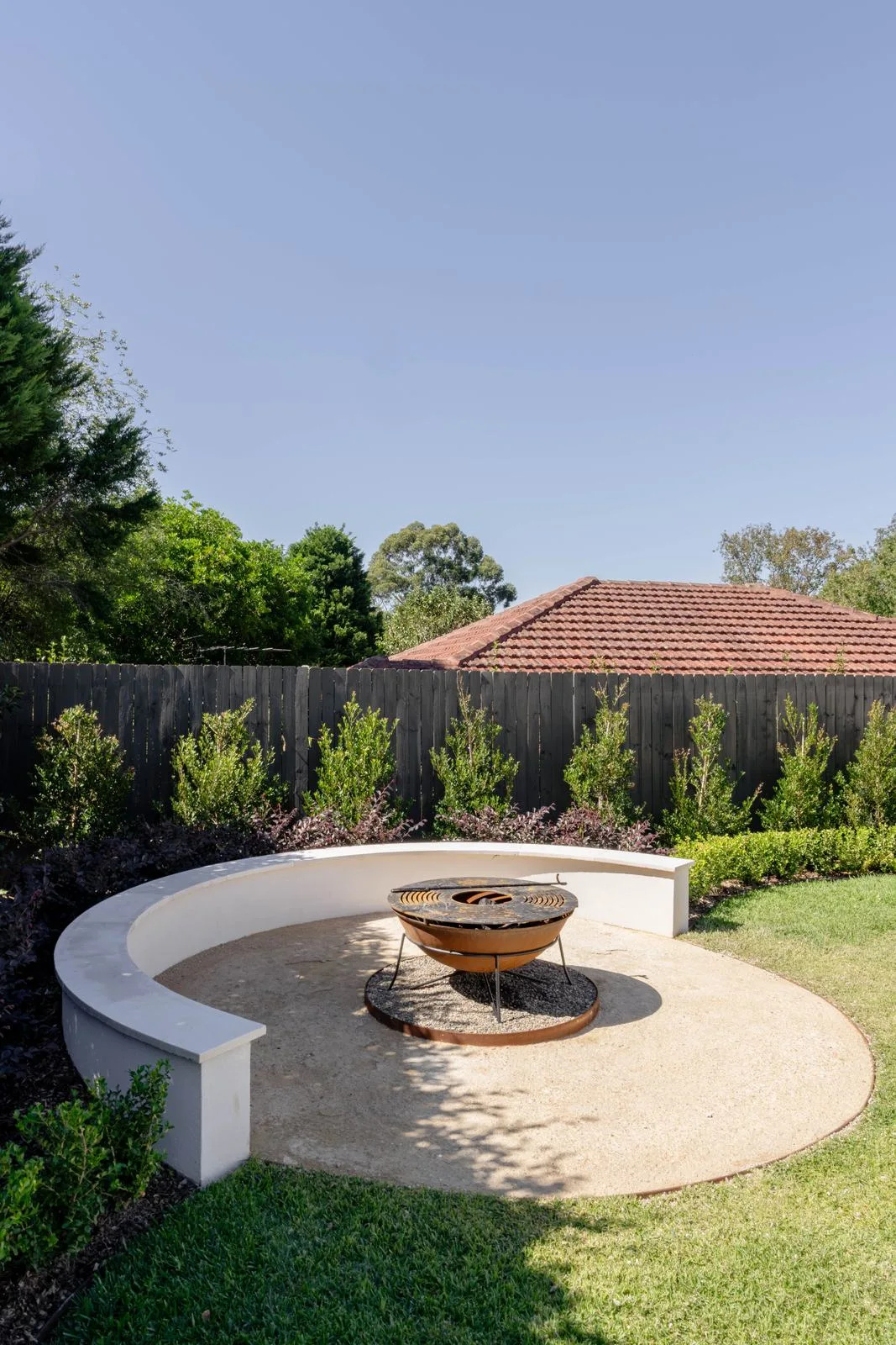Fire pit with curved rendered bench and corten steel edging on a gravel circle