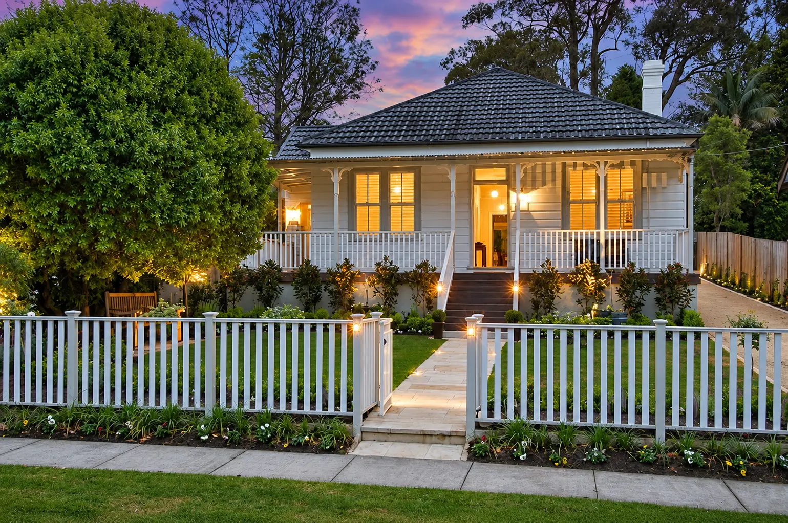 Canterbury front garden with a white picket fence, sandstone path and illuminated planting at dusk