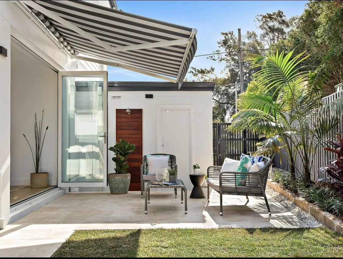 Paved alfresco terrace with lounge seating, lawn and lush planted borders