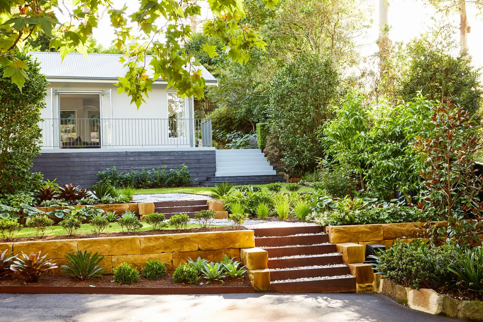 Terraced sandstone garden with tiers of planting and a broad leafy lawn