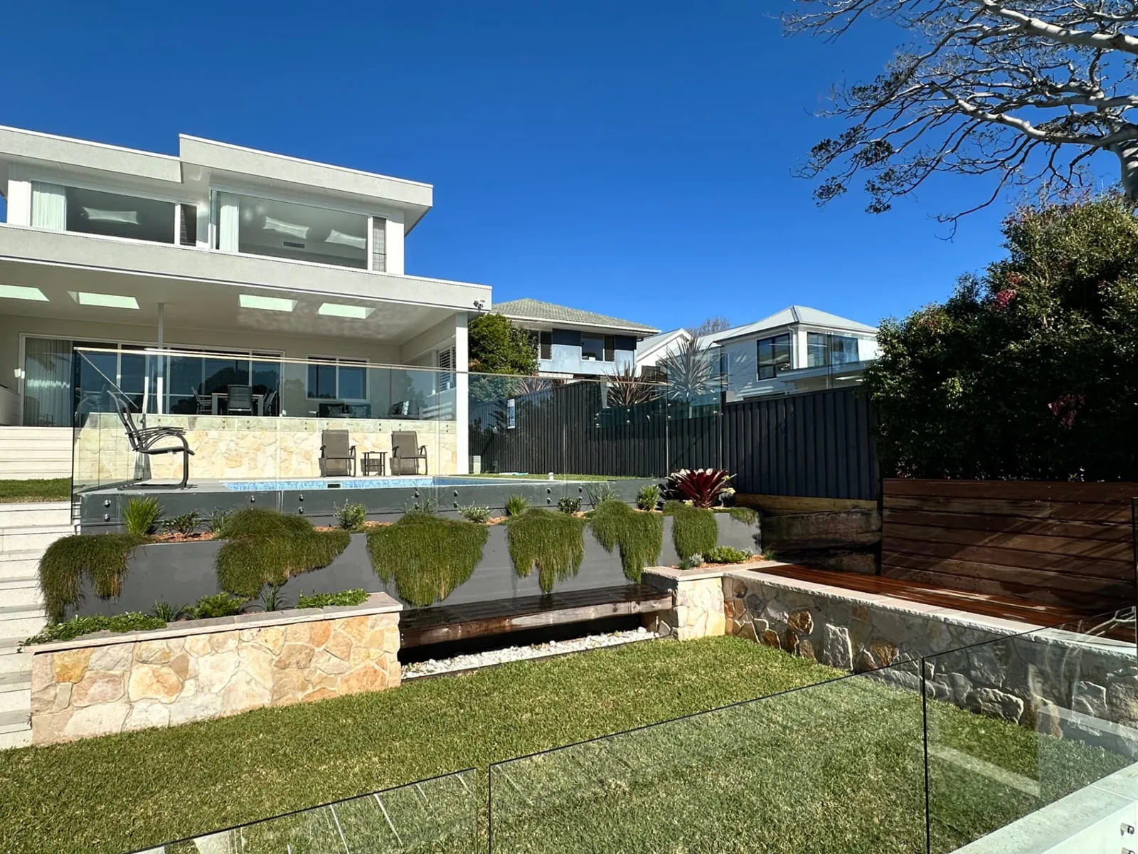 Raised swimming pool with cascading planting, sandstone retaining walls and a landscaped lawn beside a contemporary home