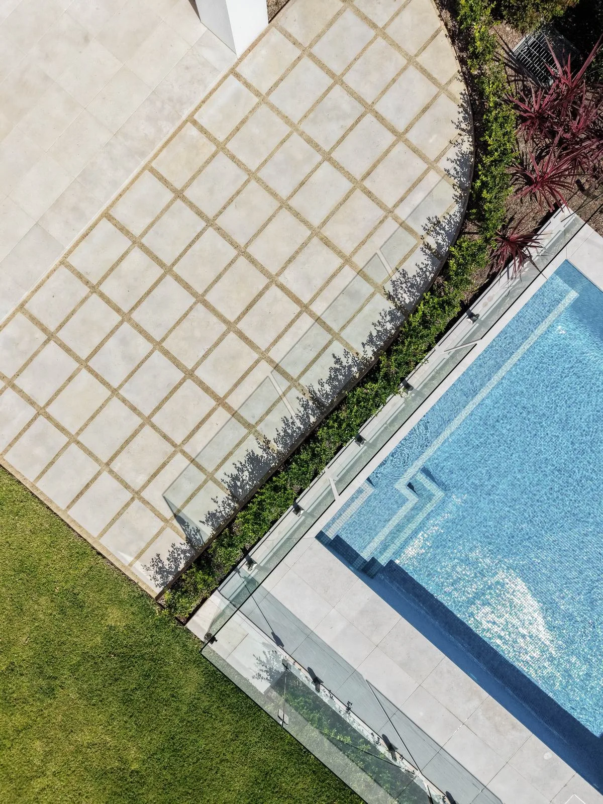 Glass pool fence and coping with layered planting and stone paving