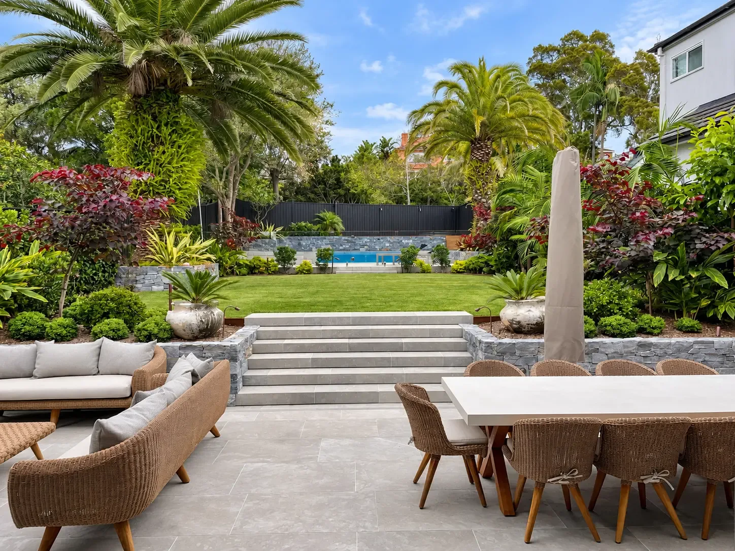 Mosman entertaining terrace with outdoor dining, broad stone steps, raised lawn and tropical planting